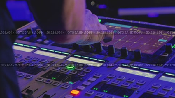A close-up of a DJ's hand adjusting the controls on a music mixing console. Bright blue and green lights emphasize the dynamic atmosphere of a live performance. Стоковое видео, видеограф Воловодов Владимир / Фотобанк Лори