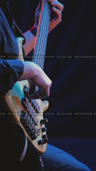 A close-up of a musician's hands skillfully playing a five-string bass guitar. In the center of attention are fingers deftly playing the strings, illuminated by stage light. Jazz concert. Стоковое видео, видеограф Воловодов Владимир / Фотобанк Лори