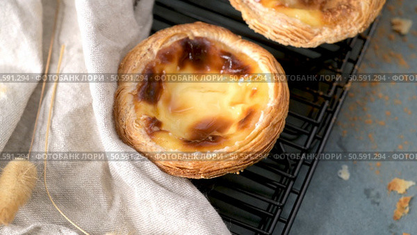 A close-up of a Portuguese custard tart with a slightly burnt top, resting on a black cooling rack next to a folded white cloth. Стоковое фото, агентство Ingram Publishing / Фотобанк Лори