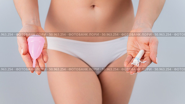 A faceless woman in cotton panties holds a pink menstrual cup and tampon on a white background. Various hygiene products during menstruation. Стоковое фото, фотограф Михаил Решетников / Фотобанк Лори