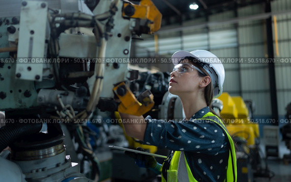 A female engineer installs a program on a robotics arm in a robot warehouse. And test the operation before sending the machine to the customer. Стоковое фото, агентство Ingram Publishing / Фотобанк Лори