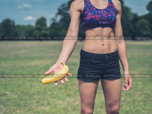A fit young woman is standing in a park and is offering a banana. Стоковое фото, агентство Ingram Publishing / Фотобанк Лори