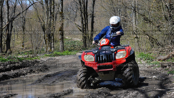 A girl driving a red quad bike rides through a puddle in the spring forest. Front view. Extreme type of outdoor activities. ATV riding. Стоковое фото, фотограф Воловодов Владимир / Фотобанк Лори