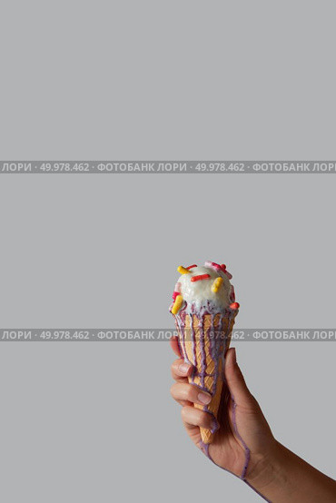 A girl’s hand holds a fruity vanilla ice cream with different pills in a waffle cone, ice cream flows over a female hand around a gray background with copy space for text.. Melting ice cream with pills in a waffle cone in a woman’s hand on a gray background with copy space. Стоковое фото, агентство Ingram Publishing / Фотобанк Лори