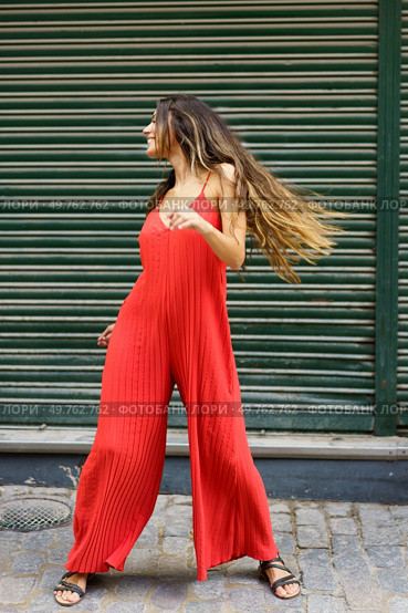 A glamorous young woman exudes confidence as she poses playfully in a trendy red jumpsuit, beautifully showcasing modern fashion against a vibrant green backdrop that complements her stylish look. A Young Woman Stylishly Poses in a Vibrant Red Jumpsuit Against a Lively Green Background. Стоковое фото, агентство Ingram Publishing / Фотобанк Лори