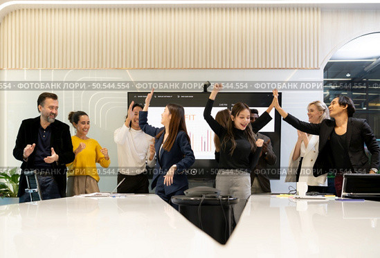 A group of multiracial businesspeople hands raise to celebrate success in front of the meeting room, indicating the concept of business success. Стоковое фото, агентство Ingram Publishing / Фотобанк Лори