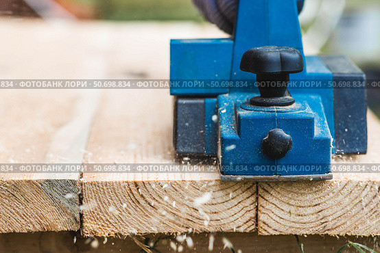 A hand-held electric planer in the hands of a craftsman. A man planing boards with an electric tool. Production of wooden products. Construction, wood processing. Стоковое фото, фотограф Photojuli / Фотобанк Лори
