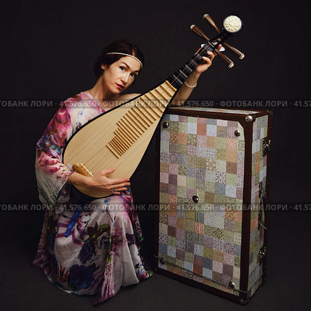 A happy female musician in Asian clothes on a studio black background. A smiling woman with a stringed musical instrument from Asia on a dark background. Стоковое фото, фотограф Андрей Журавлев / Фотобанк Лори