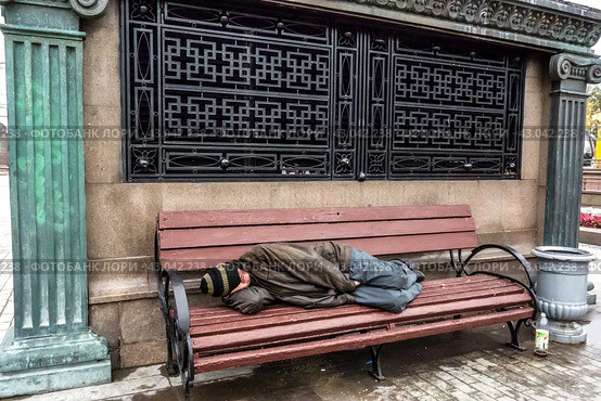 A homeless man sleeps on a bench on the street in the center of Moscow/ Бездомный бомж спит на скамейке в центре Москвы в осенний день (2016 год) Редакционное фото, фотограф Iva Noel / Фотобанк Лори