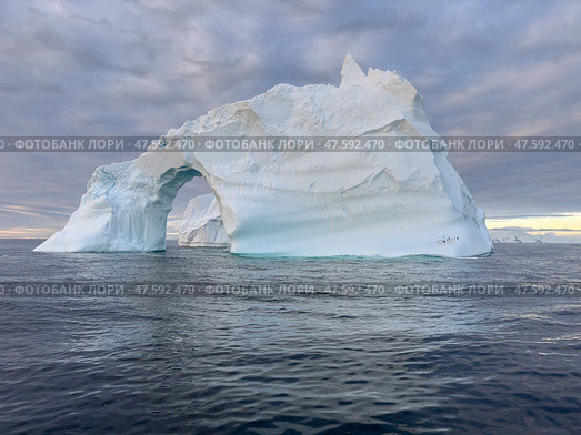 A huge high breakaway glacier drifts in the southern ocean off the coast of Antarctica at sunset, the Antarctic Peninsula, the Southern Arctic Circle, azure water, cloudy weather. Стоковое фото, фотограф Vladimir Drozdin / Фотобанк Лори