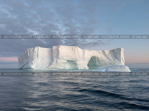 A huge high breakaway glacier drifts in the southern ocean off the coast of Antarctica at sunset, the Antarctic Peninsula, the Southern Arctic Circle, azure water, cloudy weather. Стоковое фото, фотограф Vladimir Drozdin / Фотобанк Лори