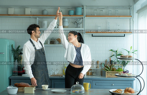 A husband wears an apron while cooking dinner with his wife. He was dancing happily before entering the kitchen to cook. Стоковое фото, агентство Ingram Publishing / Фотобанк Лори