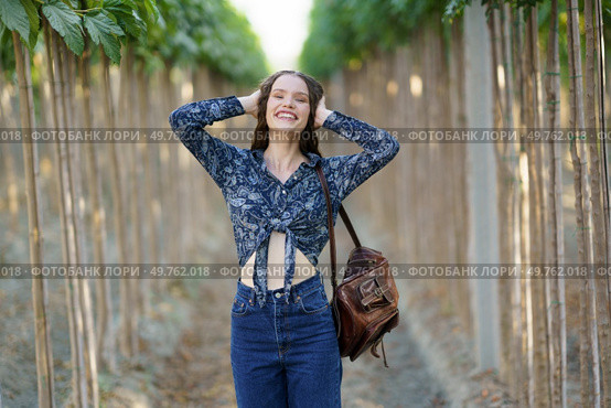 A joyful and spirited young woman poses with her arms raised in a stunning vineyard, exuding true happiness and showcasing her unique style and charm with every single smile she shares. A Joyful Young Woman is Posing Happily in a Lush Vineyard Surrounded by Natures Beauty. Стоковое фото, агентство Ingram Publishing / Фотобанк Лори