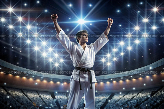 A karate athlete proudly raises his hands in the stadium in the light of spotlights and spotlights after becoming an Olympic champion. Стоковое AI-изображение, AI-художник Photojuli / Фотобанк Лори