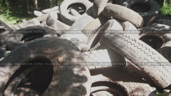 A large stack of old, dirty tires fills an empty lot under bright sunlight. The sight reveals a pressing environmental challenge regarding waste disposal and management in urban areas. Стоковое видео, видеограф Громов Александр / Фотобанк Лори