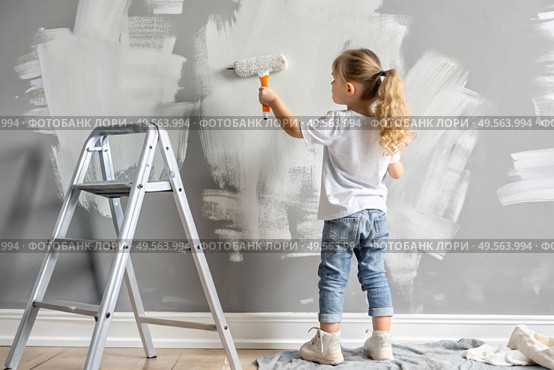 A little girl paints a wall with a paint roller in a new house. Interior decoration of the house, wall painting. Cosmetic repairs. Child labor. Стоковое AI-изображение, AI-художник Photojuli / Фотобанк Лори