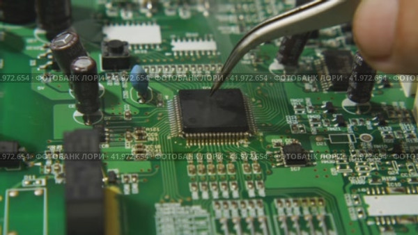 A macro video of a repairman using tweezers and a soldering station to mount the processor on the board. Underneath the microchip is boiling brazing flux. Electronics, computer,, and TV repair shop. Стоковое видео, видеограф Воловодов Владимир / Фотобанк Лори