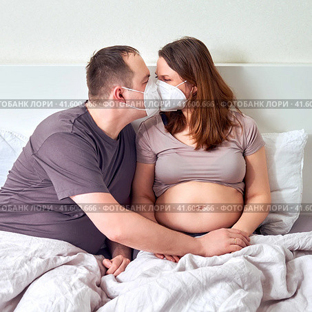 A man and a pregnant woman kiss in medical masks n95 ffp2. Coronavirus problems and excessive protection. Стоковое фото, фотограф Андрей Журавлев / Фотобанк Лори