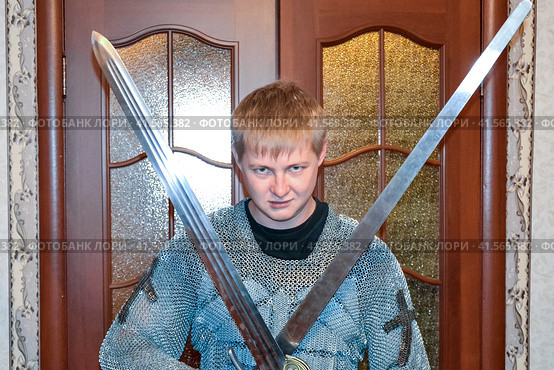 A man dressed up in a knight's hauberk at home in his room. Knight's sword in the hands of a man. Стоковое фото, фотограф Леонид Еремейчук / Фотобанк Лори