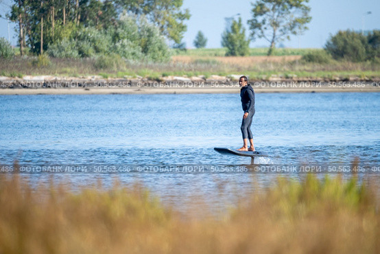 A man enjoys a peaceful ride on an electric hydrofoil surfboard near a tranquil shoreline, blending adventure with calm nature. Стоковое фото, агентство Ingram Publishing / Фотобанк Лори