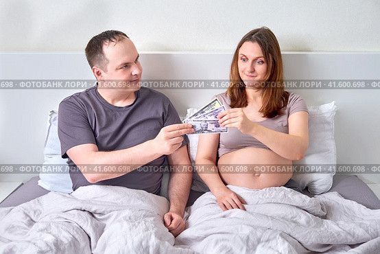 A man gives a pregnant woman money in US dollars. The husband gives his wife money bills during her pregnancy. Стоковое фото, фотограф Андрей Журавлев / Фотобанк Лори