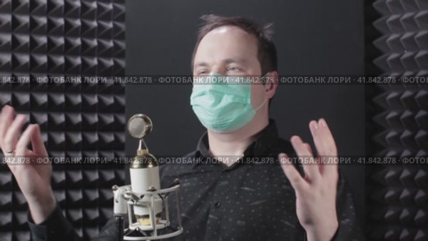 A man in a medical mask sings at a microphone in a recording studio. Quarantine in the recording studio and music small business due to problems with the virus. Стоковое видео, видеограф Андрей Журавлев / Фотобанк Лори