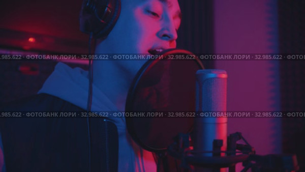 A man in hoodie rapping through the pop-filter in the microphone - sound recording studio. Стоковое видео, видеограф Константин Шишкин / Фотобанк Лори