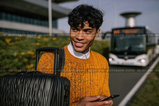 A man is smiling and holding a suitcase and a cell phone. Стоковое AI-изображение, AI-художник Ярославский Максим / Фотобанк Лори