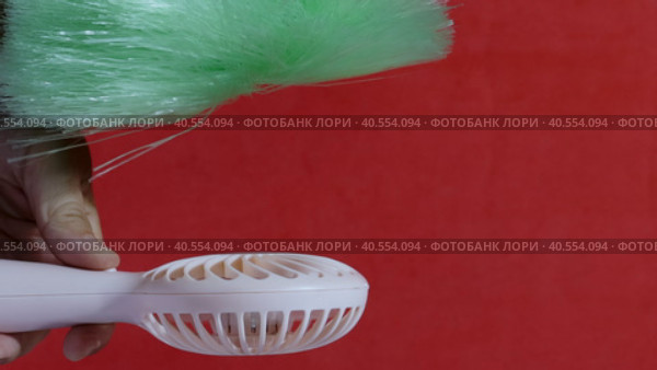 A man presses the power button on a portable portable fan. Shows operating modes. The fan blows on the brush, demonstrating the strength of the air flow. On a coral background. Close-up. Стоковое видео, видеограф Vadzim Yakubovich / Фотобанк Лори