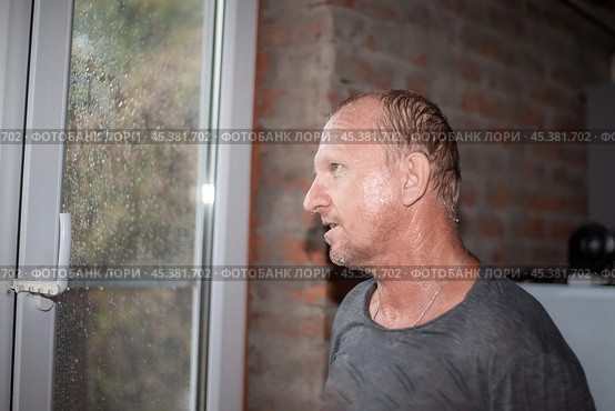A man soaked in the rain stands near the window and looks at the bad weather in autumn. Стоковое фото, фотограф Коханова Наталья / Фотобанк Лори