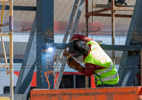 A man-welder fastens iron girders with a welding machine. Construction of the station. Стоковое фото, фотограф Юрий Поздников / Фотобанк Лори