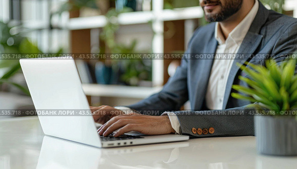 A man with a beard, wearing a hat, is seated at a table, working on his laptop computer. Стоковое AI-изображение, AI-художник Юрий Поздников / Фотобанк Лори
