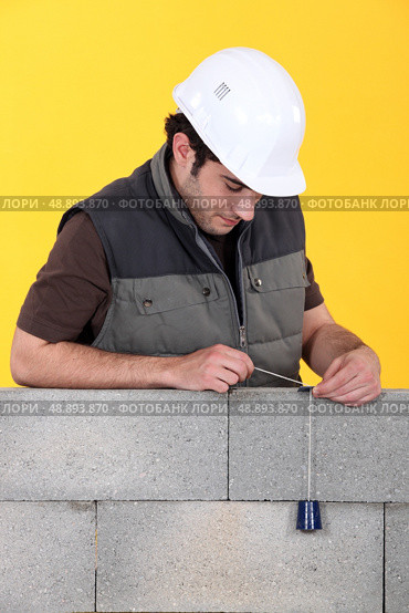 A mason using a plumb bob to check his wall. Стоковое фото, агентство Ingram Publishing / Фотобанк Лори