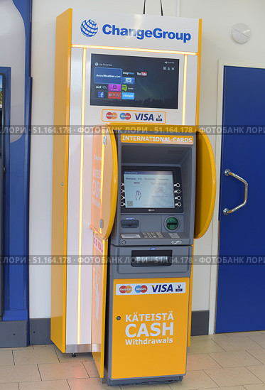 A modern ChangeGroup ATM designed for withdrawing cash from international bank cards. The device is designed in a bright yellow and gray design with inscriptions in English and Finnish. The ChangeGroup logo is located on the top panel, as well as a built-in screen where popular Internet services are visible (YouTube, Netflix, AccuWeather, etc.). The logos of the MasterCard, Visa, and Maestro payment systems stand out on the body. The ATM screen displays a welcome message asking you to insert a card. At the bottom there is a slot for cash withdrawal and receipt acceptance.The photo is suitable for topics related to banks, finance, international transfers, the use of plastic cards abroad, as well as for illustrating tourist infrastructure. (2015 год). Редакционное фото, фотограф Анна Кривицкая / Фотобанк Лори