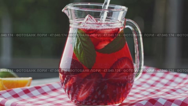 A pitcher of refreshing strawberry iced tea with mint leaves and ice cubes, set on a red and white checkered tablecloth, with slices of fruit in the background. Стоковое AI-видео, аниматор Башкирова Анна / Фотобанк Лори