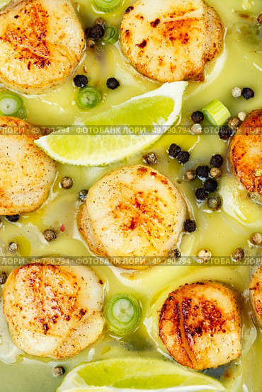 A plated dish of sea scallops garnished with fresh lime and drizzled with basil sauce. Close up. Fried scallops with sauce. Стоковое фото, агентство Ingram Publishing / Фотобанк Лори