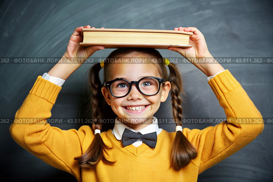 A pretty girl with glasses and books on her head. The child goes to school for the first time. A child in the classroom on the background of a blackboard. Back to school. Стоковое AI-изображение, AI-художник Photojuli / Фотобанк Лори
