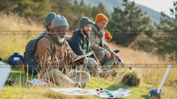 A senior African man with a beard sits on grass, reading a map. Two younger men, one with a beard and one with an orange hat, sit nearby in a natural setting. Стоковое AI-видео, аниматор Nart / Фотобанк Лори