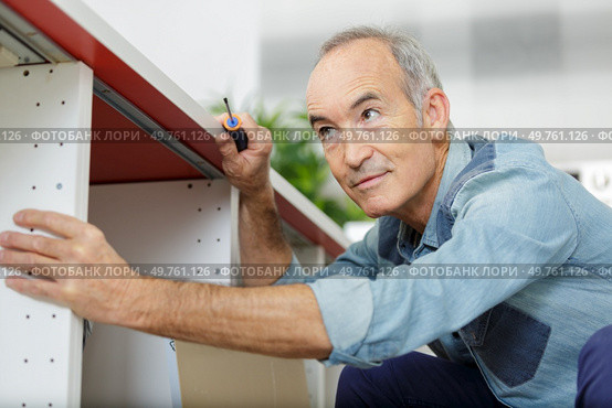 a senior man assembles furniture. Стоковое фото, агентство Ingram Publishing / Фотобанк Лори
