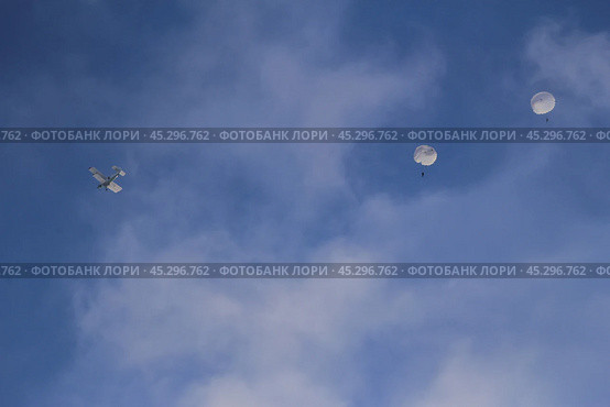 A small aircraft is seen in a bright blue sky, dispersing parachutes that drift downwards. Стоковое фото, фотограф Алексей Климкин / Фотобанк Лори