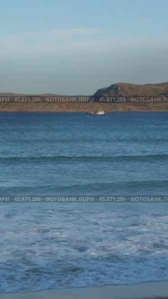 A small, lonely boat floats on a calm blue sea, with rocks as a backdrop. Vertical. Slow motion. Стоковое видео, видеограф Strunov David / Фотобанк Лори