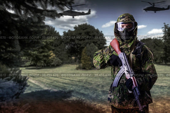 A soldier in camouflage uniform with a rifle in his hands against the background of the forest with helicopters, looks into the camera. The concept of guerrilla warfare or the game of airsoft. Стоковое фото, фотограф Владимир Арсентьев / Фотобанк Лори