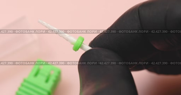 A specialist in black gloves holds in his hands a ceramic cutter for hardware manicure with a green distinctive washer, another name for a cutter is a needle for processing nails. Стоковое видео, видеограф Сергей Чайко / Фотобанк Лори