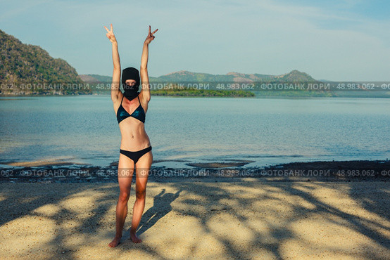A strange young woman is posing on a tropical beach in a bikini and a balaclava. Стоковое фото, агентство Ingram Publishing / Фотобанк Лори