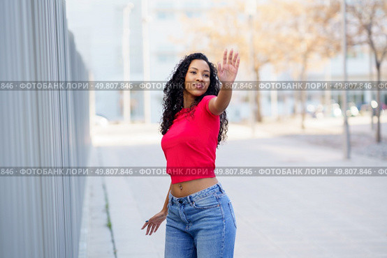 A stylish, confident young woman displays her unique fashion outdoors in a vibrant red top and trendy blue jeans, radiating positivity and inspiring others with her fun and free lifestyle. A Confident Young Woman Posing Outdoors with a Great Sense of Style and Attitude. Стоковое фото, агентство Ingram Publishing / Фотобанк Лори