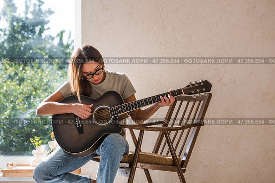 A talented young female musician sits alone and composes songs on the guitar. She plays a calm melody on a musical instrument.Music and hobbies. Стоковое фото, фотограф Photojuli / Фотобанк Лори