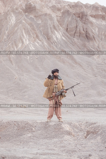 A Taliban soldier stands with a machine gun, In the desert mountain landscape. Стоковое фото, агентство Ingram Publishing / Фотобанк Лори