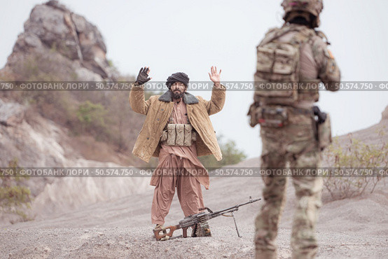 A Taliban soldier stands with a machine gun, Raise hands in surrender to the allied soldiers, In the desert mountain terrain battlefield. Стоковое фото, агентство Ingram Publishing / Фотобанк Лори