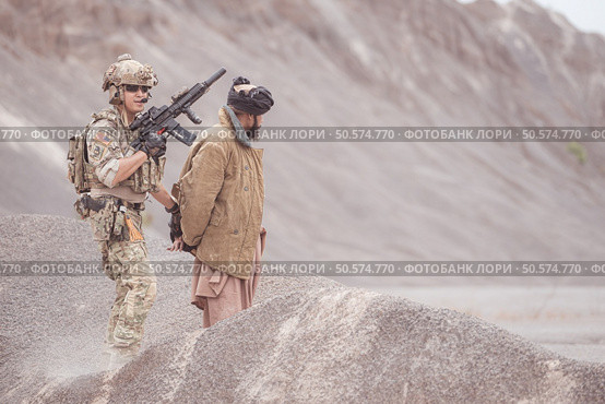 A Taliban soldier stands with a machine gun, Raise hands in surrender to the allied soldiers, In the desert mountain terrain battlefield. Стоковое фото, агентство Ingram Publishing / Фотобанк Лори