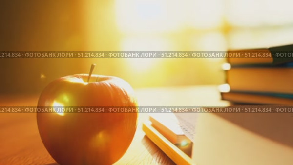 A vibrant red apple rests on a wooden table next to books and pencils, illuminated by warm afternoon sunlight streaming through the window. Стоковое AI-видео, аниматор Данила Большаков / Фотобанк Лори
